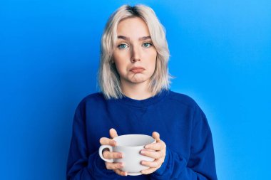 Bir fincan kahve içen genç sarışın kız üzgün ve endişeli, sinirli ve korkmuş. hüzünlü ifade. 