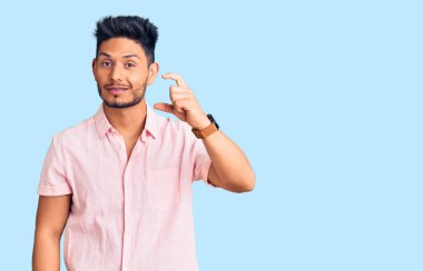 Yakışıklı Latin Amerikalı genç adam rahat bir yaz gömleği giyiyor gülümsüyor ve kendinden emin el hareketleriyle küçük boy işareti yapıyor parmakları bakıyor ve kameraya bakıyor. ölçüm kavramı. 