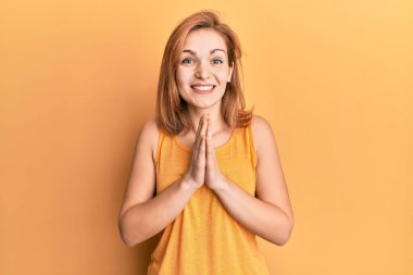 Sıradan giyinmiş, kolsuz tişörtlü, elleri kolları bağlı, af dileyen, kendinden emin, gülümseyen beyaz bir kadın.. 