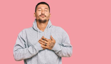 Dövmeleri olan, sıradan bir kazak giyen, elleri göğsünde, gözleri kapalı ve yüzünde minnet ifadesi olan yakışıklı bir adam. sağlık kavramı. 