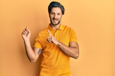 Gündelik sarı tişört giyen genç İspanyol adam gülümsüyor ve kameraya bakıyor iki eliyle ve parmaklarıyla kenarı işaret ediyor.. 