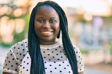 Genç Afrikalı Amerikalı kadın gülümseyerek şehirde mutlu mesut duruyor..