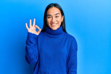 Kış süveteri giyen genç Asyalı kadın gülümsüyor. El ve parmaklarıyla 