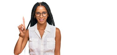 Güzel İspanyol kadın, günlük kıyafetler ve gözlük takıyor. Bir numaralı parmağını gösteriyor ve işaret ediyor. Kendinden emin ve mutlu bir şekilde gülümsüyor.. 