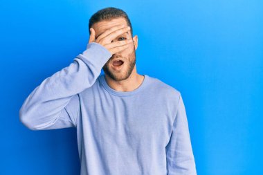 Gündelik giysiler giymiş genç beyaz bir adam. Şoka girip yüzünü ve gözlerini eliyle kapatıyor. Korkmuş parmaklarından bakıyor. 