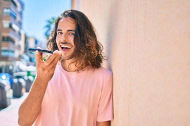 Genç İspanyol adam gülümsüyor. Akıllı telefonda konuşuyor. Duvara yaslanıyor.