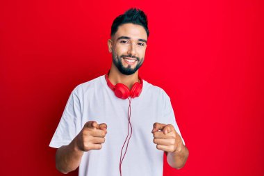 Sakallı genç adam müzik dinliyor kulaklıkla kamerayı mutlu ve komik yüzüyle işaret ediyor. iyi enerji ve titreşimler. 