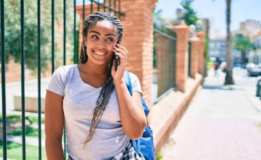 Genç Afrikalı Amerikalı öğrenci kampüste akıllı telefon kullanarak mutlu bir şekilde gülümsüyor.