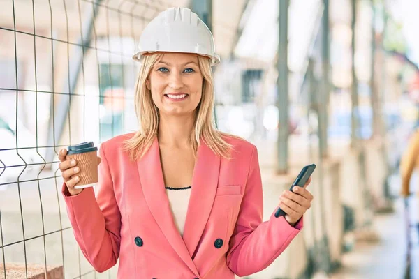 Young caucasian architect woman using smartphone and drinking coffee at the city