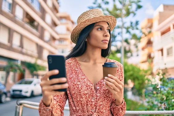 African american tourist woman with serious expression using smartphone and drinking coffee at the city.