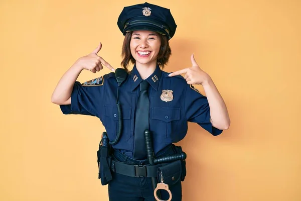 Young beautiful woman wearing police uniform looking confident with smile on face, pointing oneself with fingers proud and happy.