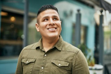 Genç Latin adam gülümseyerek şehirde mutlu mesut dikiliyor..