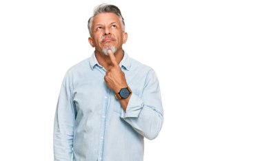 Orta yaşlı, gri saçlı, günlük kıyafetler giyen, şüpheyi düşünen, çenesinde parmak olan ve kafasını kaldırıp merak eden bir adam. 