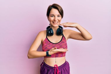Kısa saçlı, spor giyimli, kulaklık takan, büyük ve büyük boylarda işaret eden esmer bir kadın. Kameraya bakıp gülümsüyor. ölçüm kavramı. 