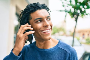 Genç Afrikalı Amerikalı gülümseyen mutlu bir adam şehrin caddesinde akıllı telefondan konuşuyor..