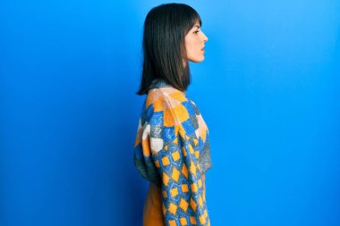 Günlük kışlık kazak giyen genç İspanyol kadın yan tarafa bakıyor, rahat poz veriyor kendine güvenen bir gülümsemeyle doğal bir yüz ifadesi sergiliyor.. 