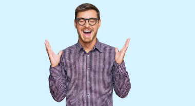 Yakışıklı beyaz bir adam, günlük kıyafetler ve gözlük takmış, çılgın ve çılgın başarısını kutluyor, kolları havada ve gözleri kapalı, heyecanlı çığlıklar atıyor. Kazanan konsept 