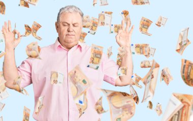 Kıdemli, gri saçlı, günlük kıyafetler giyen, gözleri kapalı gülümseyen, parmaklarıyla meditasyon yapan bir adam. yoga konsepti.