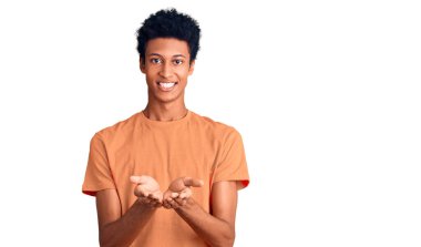 Elleri avuçlarında gülümseyen ve el hareketi yapan gündelik giysiler giyen genç Afro-Amerikan bir adam. Bekleme ve koruma 