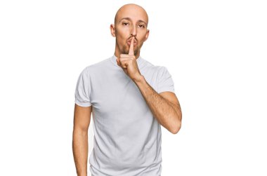 Kel, sakallı, beyaz tişörtlü, dudakları parmaklı, sessiz olmak isteyen bir adam. sessizlik ve gizli konsept. 