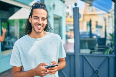 Genç İspanyol adam şehirde akıllı telefon kullanarak mutlu gülümsüyor..