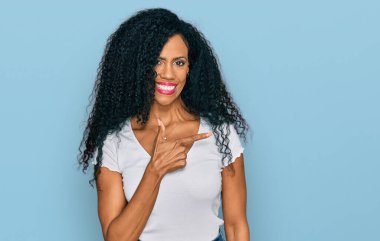 Orta yaşlı Afro-Amerikalı kadın, günlük beyaz tişört giyiyordu. Neşeli, yüzünde mutlu ve doğal bir ifadeyle, elleri ve parmaklarıyla yüzünü gösteren bir gülümseme vardı. 