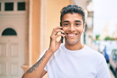 Genç Latin adam gülümsüyor ve şehirde akıllı telefondan konuşuyor..