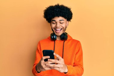 Afro saçlı genç Afro-Amerikalı adam akıllı telefon kullanarak çılgınca kutlama yapıyor ve başarıya hayret ediyor gözleri açık heyecanla bağırıyor.. 