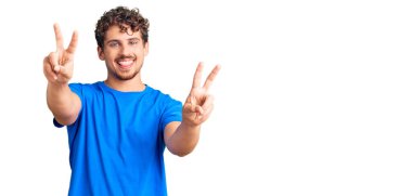 Kıvırcık saçlı, sıradan kıyafetler giyen, dili dışarı fırlamış ve zafer işareti yapan genç yakışıklı bir adam. İki numara.. 