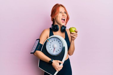 Kilo kaybetmeyi dengelemek için elinde ağırlık makinesi tutan genç ve güzel kızıl saçlı kadın kızgın ve öfkeli çığlıklar atıyor. Öfkeyle bağırıyor.. 