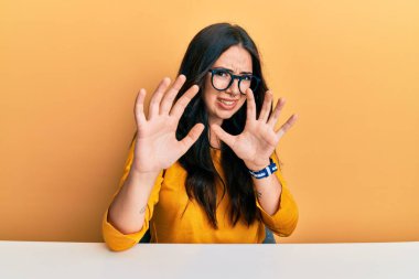 Güzel, esmer, gözlüklü, sıradan kıyafetler giyen bir kadın. İğrenme reaksiyonu yüzünden tiksinti ve tiksinti dolu bir ifadeyle masada oturuyor. Eller havada. 