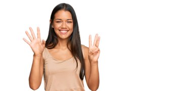 Güzel İspanyol kadın gündelik kıyafetler giyer ve sekiz numaralı parmaklarıyla gülümseyerek mutlu ve kendinden emin bir şekilde işaret eder.. 