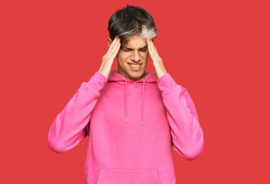 Genç İspanyol adam, stresten dolayı kafasında ağrı olsun diye elleri kafasında pembe bir kazak giyiyor. migren ağrısı. 