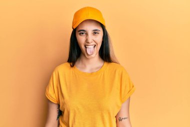 Teslimat üniforması giyen ve şapkalı genç İspanyol kadın komik bir ifadeyle mutlu bir şekilde dilini dışarı çıkarıyor. duygu kavramı. 