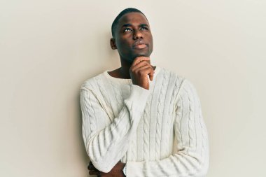 Elleri çenesinde gündelik giysiler giyen genç Afro-Amerikan bir adam soru soruyor, düşünceli bir ifade. Gülümseyen ve düşünceli bir yüz. şüphe kavramı. 
