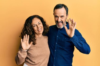 Orta yaşlı İspanyol çift gündelik giysiler giyip selam veriyor mutlu ve gülümsüyor, dostça karşılama jestleri yapıyor. 