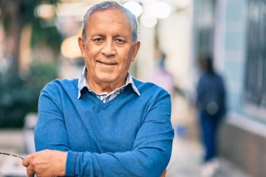 Yaşlı, gri saçlı, kollarını kavuşturmuş, gülümseyen, mutlu bir adam..