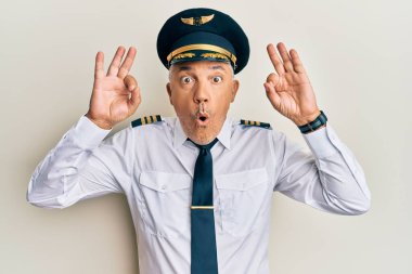 Yakışıklı, olgun, uçak pilotu üniforması giyen bir adam. Şaşırmış ve şaşırmış görünüyor. Parmaklarıyla onay sembolü yapıyor. çılgın ifade 