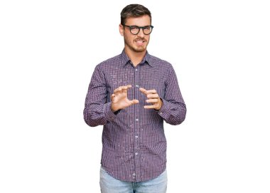 Sıradan kıyafetler ve gözlük takan yakışıklı beyaz adam tiksindirici bir ifade takınıyor ve tiksinti reaksiyonu yüzünden tiksindirici ve korkunç bir ifade takınıyor. Eller havada. 