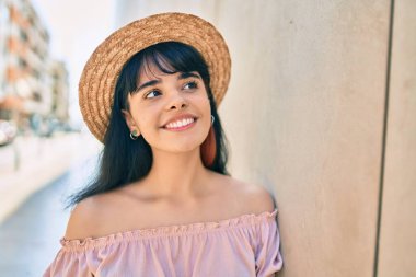 Latin kökenli genç bir turist yaz stili giyiniyor ve şehrin duvarına yaslanıyor..