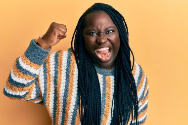 Örgülü genç siyahi bir kadın, öfkeyle bağırırken kızgın, kızgın ve kızgın bir şekilde elini kaldırıyor. öfke ve agresif konsept. 