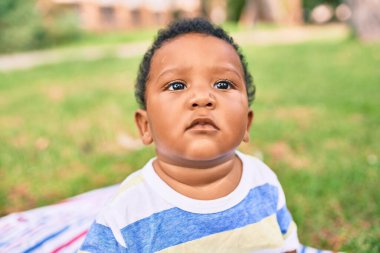 Sevimli Afro-Amerikan tombul çocuk parkta çimlerin üzerinde oturuyor..