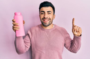 Elinde şampuan şişesi olan genç İspanyol bir adam bir fikirle gülümsüyor ya da bir soru işareti yapıyor. 