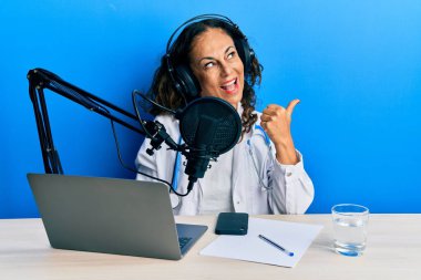 Güzel orta yaşlı bir doktor, radyo stüdyosunda çalışıyor. Gülümsüyor, gülümsüyor ve baş parmağıyla yan tarafa bakıyor.. 