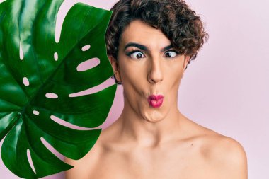 Genç adam yeşil bitki yaprağını güzel yüzüne yakın tutarak makyaj yapıyor. Ağız ve şaşı gözlerle balık yüzü yapıyor. Çılgınca ve komik.. 