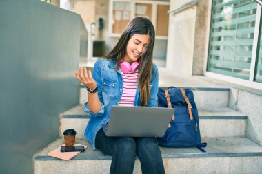 Genç İspanyol öğrenci gülümseyerek üniversitede bilgisayarla video araması yapıyor..