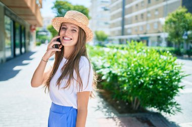 Tatilde gülümseyen genç sarışın kadın şehrin caddesinde akıllı telefondan konuşuyor.