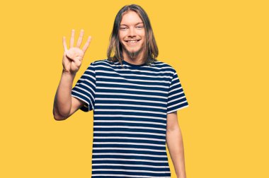 Uzun saçlı yakışıklı beyaz bir adam. Sıradan çizgili tişört giyiyor. Dört numarayı gösteriyor ve gülümsüyor.. 