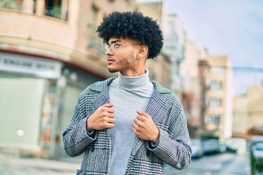 Genç Afro-Amerikan iş adamı ciddi bir ifadeyle şehirde duruyor..