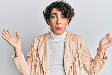 Kadın makyajı yapan genç bir adam ve kadın kıyafetleri, habersiz ve kolları açık, hiçbir fikrim yok ve şüpheli bir yüzüm var.. 